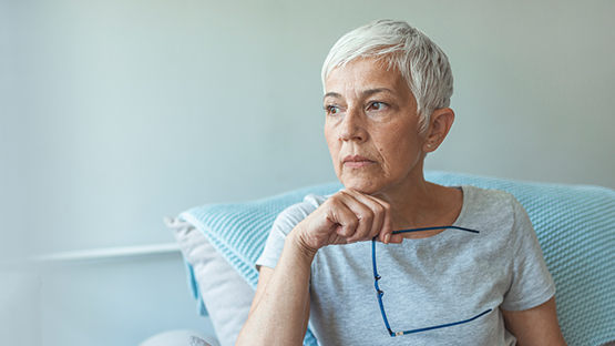 An older woman with white hair in a hospital bed looking off camera while holding her glasses, as she waits for her procedure for heart failure.