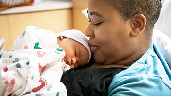 A mother gently laying her newborn who is wrapped in blankets, in the nursery.