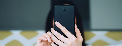 A woman sitting on a couch holding a phone that is blocking her face and looking for a doctor on our Find Care website.