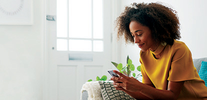 A woman using her phone to find AHN contact information to find her a doctor, while sitting on a couch.