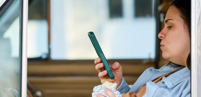 A man in shorts sitting on a couch with an icepack on his left leg while scheduling an appointment on his phone.