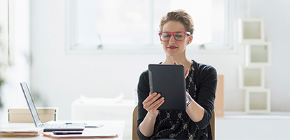 A smiling woman with bright red glasses using her tablet for an AHN telehealth visit.