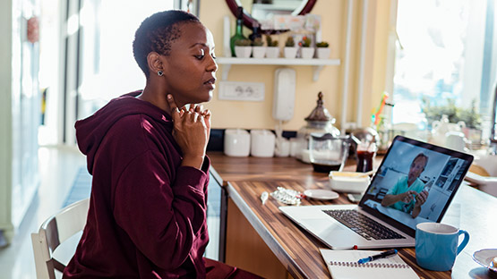 A woman checking her pulse during a telehealth video visit with her doctor.