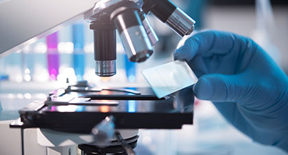 A lab technician looking at a flat glass slide that they are putting into a microscope.