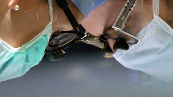 Closeup view of two neurosurgery residents wearing surgical loupes and leaning over a patient during surgery.