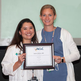 A resident and her mentor holding up a diploma that they won.