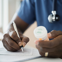 A doctor writing a prescription while holding a prescription bottle.