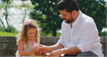 A father and daughter sitting next to each other outside holding an ice cream