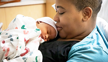 A new mom laying in a hospital bed with her newborn who is wrapped in a blanket.