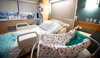 A view of a hospital room with an empty hospital bed and empty bassinet.