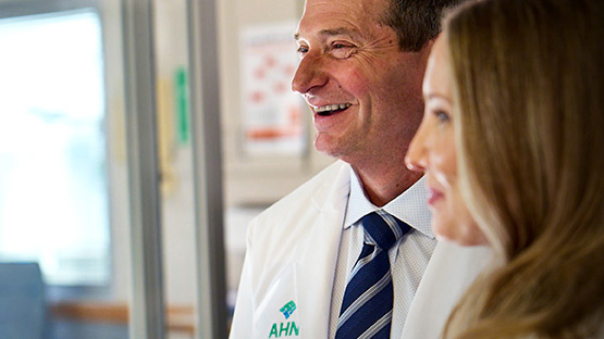 A doctor in a lab coat smiles while talking with a patient