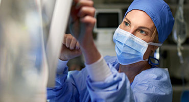 A doctor in surgical gear in an operating room checking a monitor