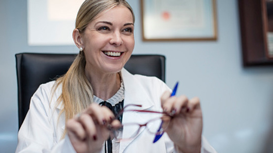 A medical professional smiling while looking off camera and holding her glasses