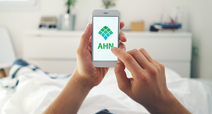 A person's hands holding a phone displaying AHN's website.