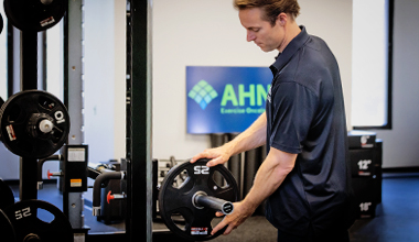 A medical professional in a dark blue polo shirt puts a weight on a barbell.