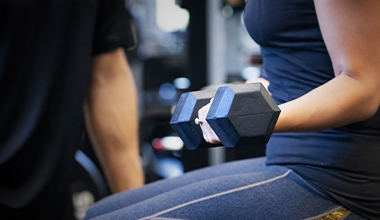 A person in blue workout clothes lifts a dumbbell in a gym.