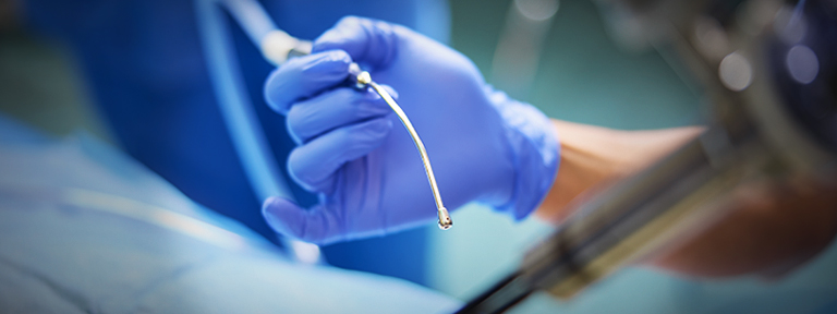 A medical professional in blue gloves holds a small curved tool during a procedure.