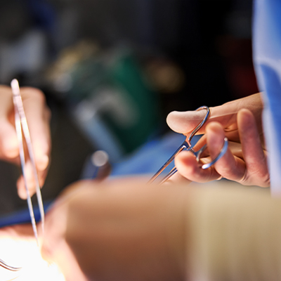 Two sets of hands, one holding forceps, carefully use surgical tools during an operation.