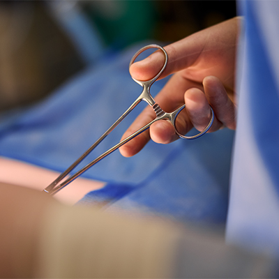 A medical professional in blue scrubs holds shiny surgical scissors during an operation.
