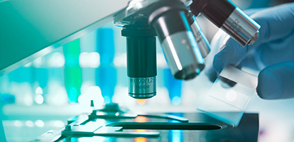 A lab technician placing a flat glass slide into a microscope so that they can look at it.