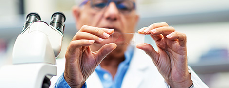 A lab technician examining a flat glass slide that he is about to place into a microscope.