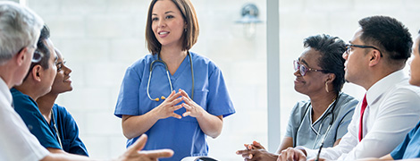 A doctor speaking to a group of her colleagues who are sitting around a conference table.