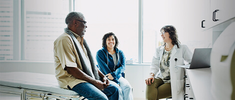 Doctor shares information on a laptop with a man and a woman in an exam room during a healthcare consultation