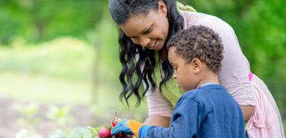 A woman holding radishes in a garden with the help from her son, she is happy after receiving care at AHN for her chronic health condition.