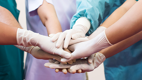 A group of medical professionals doing a huddle and a hand stack together, as they prepare to treat a patient for their chronic illness.