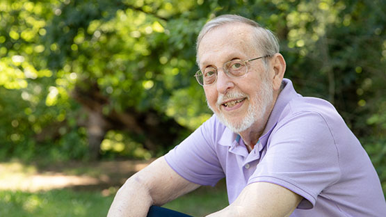 o	AHN patient Carleton Weber smiling while looking into the camera as he is sitting outside on a bench.