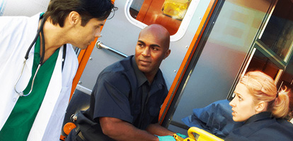 A doctor meeting EMTs at their ambulance as they are unloading their stretcher.