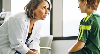 A doctor talking to a young student athlete in an exam room.