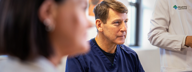 A medical professional in blue scrubs looks forward during a consultation.