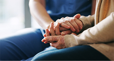 A medical professional holds an elderly person's hands, offering comfort and support.