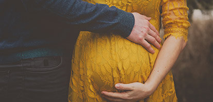 A woman in a yellow dress holding her pregnant belly.