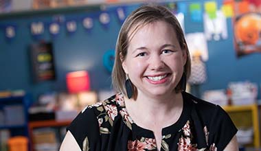 Cancer survivor, AHN patient, and teacher KD Meucci smiling at the camera as her photo is taken in her classroom.